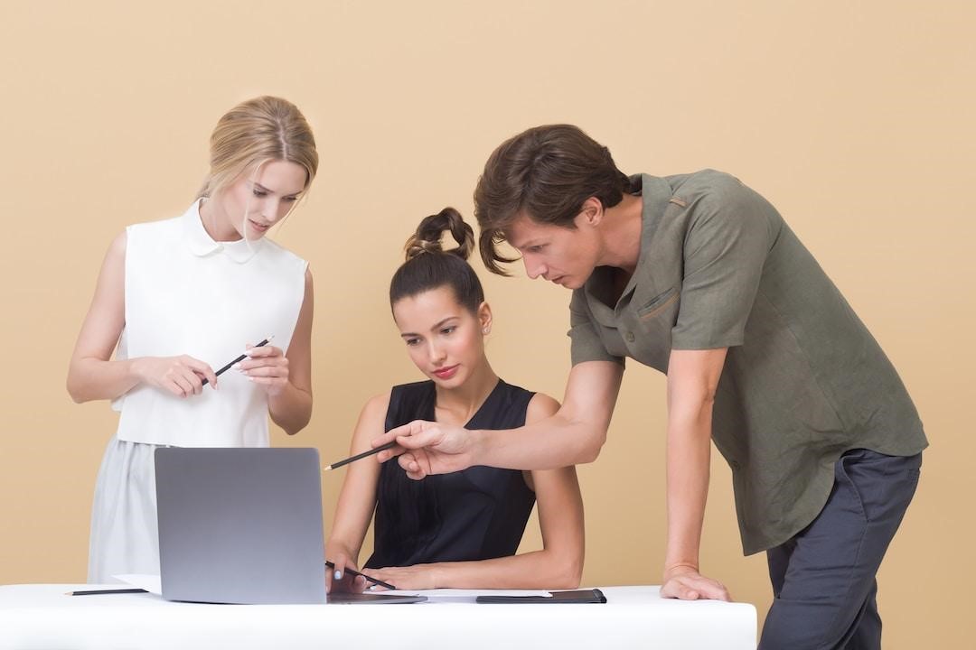 Three people looking at a laptop screen discussing the proposal management process.